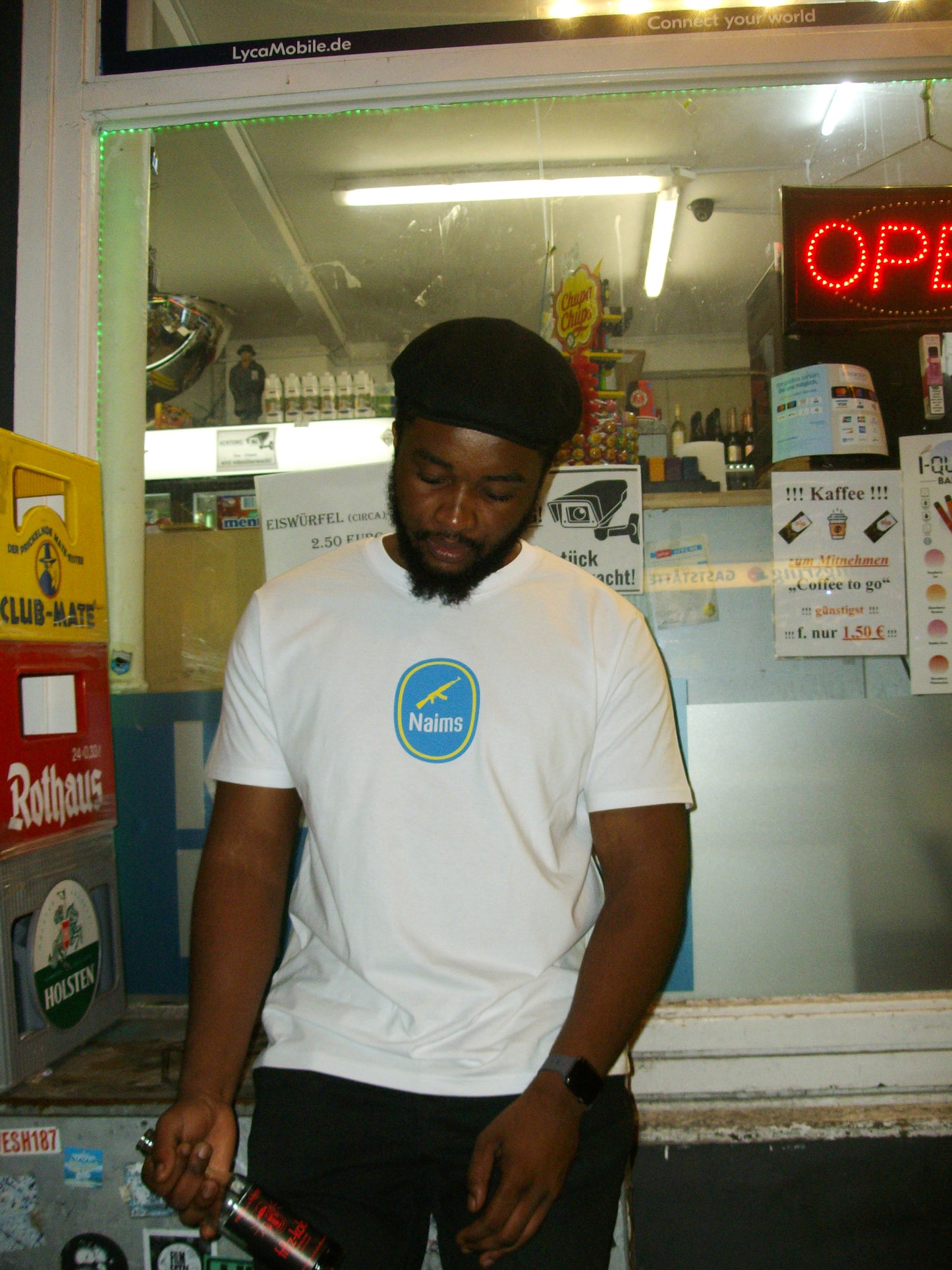 Model wearing the Don't Trip Tee - White NAIMS premium cotton t-shirt with a bold blue front logo, styled in an urban night-time setting banana resistance symbol