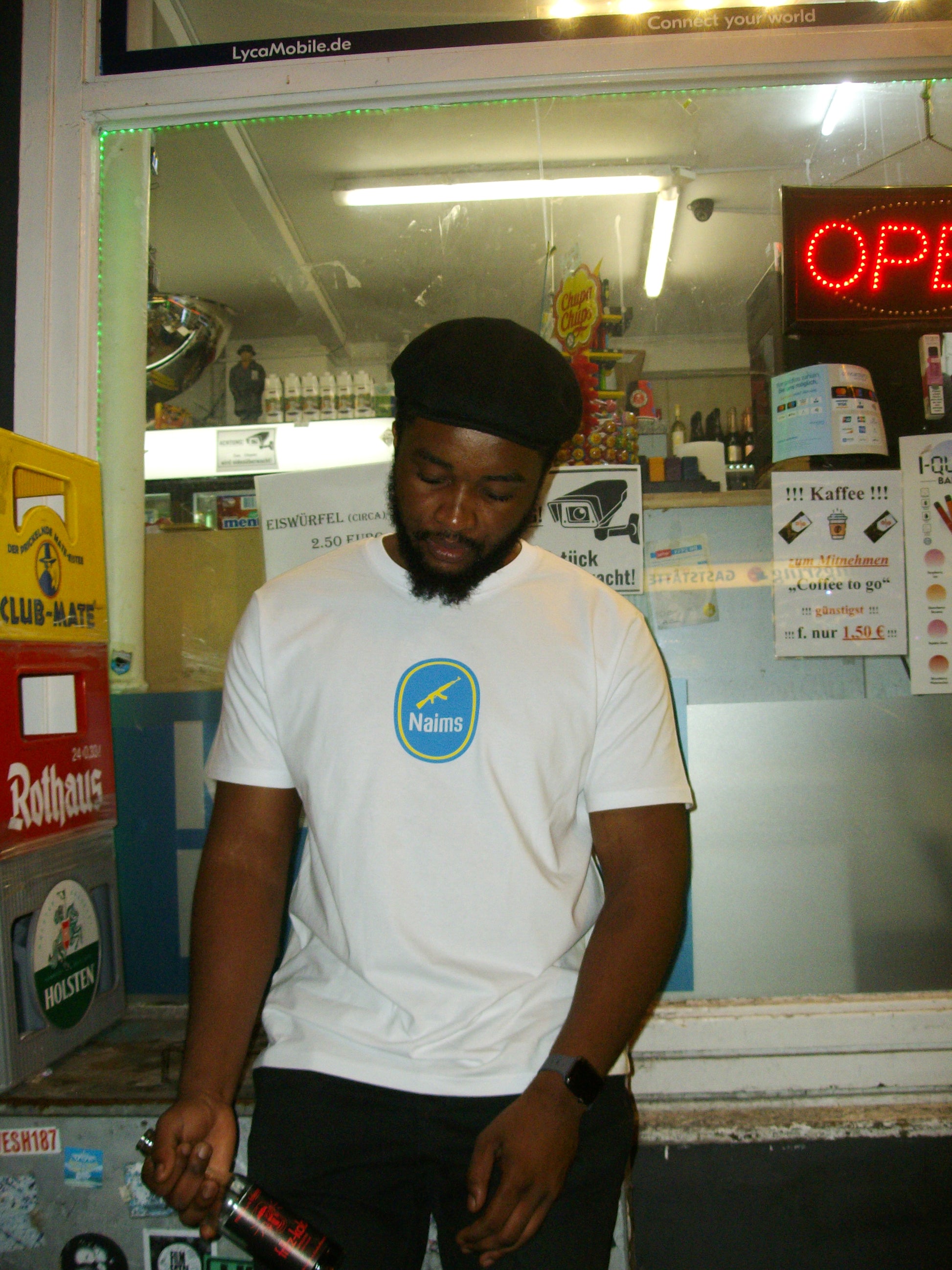 Model wearing the Don't Trip Tee - White NAIMS premium cotton t-shirt with a bold blue front logo, styled in an urban night-time setting banana resistance symbol