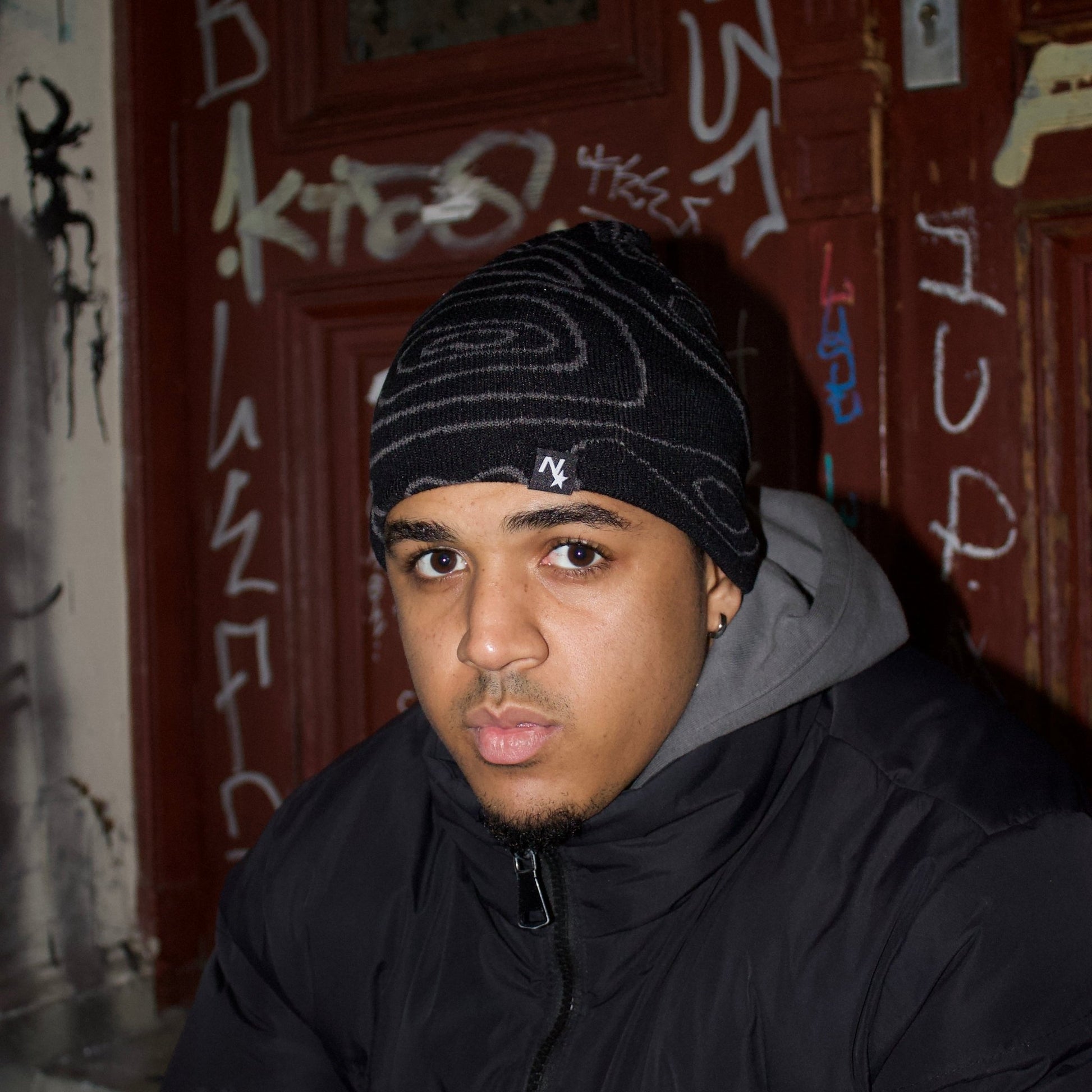 Model wearing the black NAIMS beanie with abstract embroidered geographical map pattern – a versatile knit cap for urban streetwear fashion